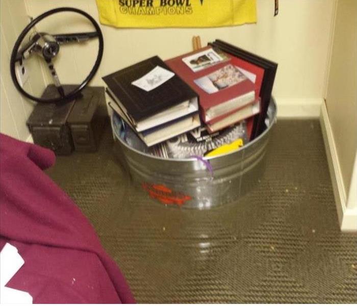 room with tan carpet covered in water damage with a bucket of books