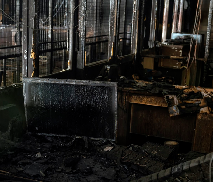 a fire damaged office with soot covering the desks and computers and debris covering everything